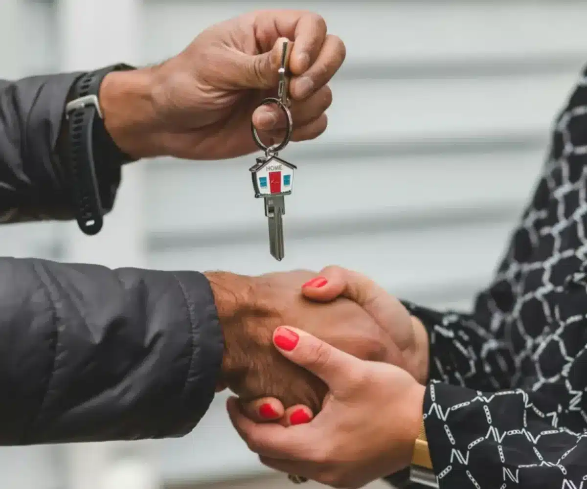 A person handing over house keys to a new owner with a handshake.